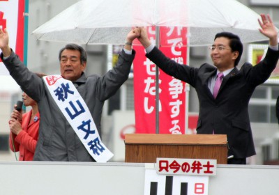 聴衆の声援にこたえる（左から）秋山文和県議候補と山下芳生書記局長＝2015年4月5日、春日部市